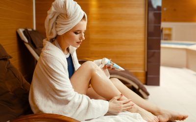 Sexy girl in bathrobe and towel on the head applying cream in spa chair, body care. Relaxation leisure, healthy lifestyle, attractive woman resting in armchair, beauty salon